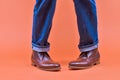 Closeup of Crossed Feet of Men In Stylish Tanned Leather Brown Brogued Boots On Standing Man Wearing Jeanswear Against Orange