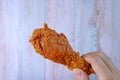 Crunchy Fried Chicken Drumstick in Hand with Blurry Wooden Wall in Backdrop