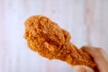 Crunchy Fried Chicken Drumstick in Hand with Blurry Wooden Wall in Background