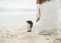 Closeup on cup of beverage near woman in sweater sitting on beach Royalty Free Stock Photo