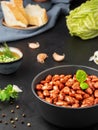 Closeup of a cup with boiled red beans decorated with basil leaves. Healthy vegetarian dish, next to a bowl of spices, bread and a Royalty Free Stock Photo