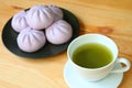 Closeup a cup of green tea with blurry pile of purple sweet potato steamed buns on wooden table