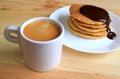 Cup of hot coffee with blurry pancake with chocolate ganache sauce in background