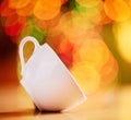 Closeup of a cup isolated against a colourful bokeh background. White teacup tilted on the side on a table. Crockery to