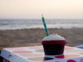 Closeup of a cupcake with stripped candle and blurred background of sand beach