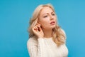 Closeup curious nosy blond woman in white sweater holding hand near ear trying to hear secret information, overhearing private