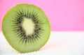 Closeup of cut half, sliced fresh kiwi isolated on white cotton sheet, overlay with bokeh, blurred acrylic pink background.