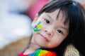 Closeup of cute Asian girl face sitting on chair made of wood. Watercolors are cartoon flower on skin of kid.