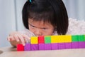 Closeup cute Asian girl playing with colorful wooden cube. Child intently aims at placement of wooden blocks.