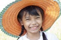 Closeup Asian little girl wearing a straw hat is standing smiling and looking at the camera in the garden. Royalty Free Stock Photo