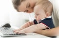 Closeup of cute baby sitting on mothers lap and typing on keyboard Royalty Free Stock Photo