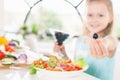 Closeup cute little girl making salad. Holding olive. Child cooking. Royalty Free Stock Photo