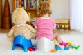 Closeup of cute little 12 months old toddler baby girl child sitting on potty. Kid playing with big plush soft toy Royalty Free Stock Photo