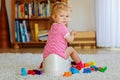 Closeup of cute little 12 months old toddler baby girl child sitting on potty. Kid playing with doll toy. Toilet Royalty Free Stock Photo