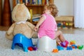 Closeup of cute little 12 months old toddler baby girl child sitting on potty. Kid playing with doll toy. Toilet Royalty Free Stock Photo