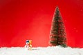 Closeup of a cute snowman toy on fae snow with a Christmas tree on it against a red background Royalty Free Stock Photo