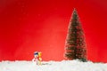 Closeup of a cute snowman toy on fae snow with a Christmas tree on it against a red background Royalty Free Stock Photo