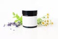 Closeup of dark glass jar with blank paper label. Mint leaves, lavender and feverfew flowers on white table backround