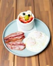 Closeup of delicious breakfast with fried eggs and bacon slices with fruit salad on a wooden table Royalty Free Stock Photo