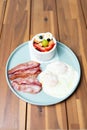 Closeup of delicious breakfast with fried eggs and bacon slices with fruit salad on a wooden table Royalty Free Stock Photo