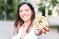 Closeup of delicious and colorful donut in hand of a woman defocused in city park. junk sweet and tasty fast food dessert