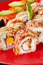 Closeup of unagi rolls with grilled eel, cream cheese, orange pulp and sesame on red plate