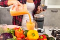 Closeup details in the kitchen couple in the morning pouring a healthy orange smoothie on a big glass Royalty Free Stock Photo