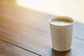 Closeup of disposable takeaway paper cup of hot coffee latte with milk foam on wooden table Royalty Free Stock Photo