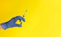 Closeup of doctor hand in blue glove holding plastic syringe on yellow background. Medical injection. Covid-19 vaccination Royalty Free Stock Photo