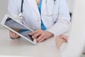 Closeup of a doctor and patient sitting at the desk. Physician pointing into tablet pc. Medicine and health ca Royalty Free Stock Photo