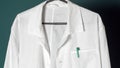 Closeup of a doctor`s white lab coat on a hanger against a dark background.