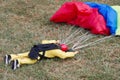 Closeup of a doll lying on a lush green lawn with colorful parachutes in its grasp