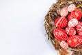 Closeup Easter red eggs with folk white pattern inside bird nest on white. Top view Royalty Free Stock Photo