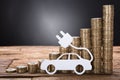 Electric Car Against Stacked Coins On Wooden Table