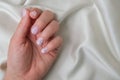 Closeup elegant pastel natural modern design manicure on fabric silk background. Female hands. Gel nails. Nude manicure. Beige Royalty Free Stock Photo