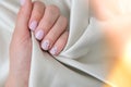 Closeup elegant pastel natural modern design manicure on fabric silk background. Female hands. Gel nails. Nude manicure