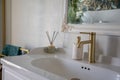 Closeup elegant sink with gold faucet, marble countertop and ceramic basin, reed diffuser and soft mirror reflection Royalty Free Stock Photo