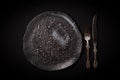 Closeup empty round black aged ceramic plate, vintage cutlery - fork, knife on dark background with copy space. Concept Royalty Free Stock Photo
