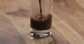 Closeup espresso pour into glass with cold water on wood table