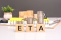 ETA text in wooden blocks with coins stacked in increasing stacks. Estimated Time Of Arrival concept