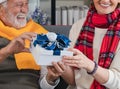 Exchanging Christmas present or gift in hands of happy Caucasian senior couple during the day at home. Christmas and New Year