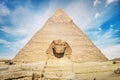 A closeup of the face of the Great Sphinx with pyramid in the background on a beautiful cloudy blue sky day in Giza, Cairo, Egypt