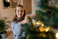 Closeup face of happy adorable little girl enjoying process of decorating Christmas tree at home. Cute smiling child