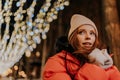 Closeup face of pretty frozen young woman in hat and winter jacket warming hands in cold winter night standing posing on Royalty Free Stock Photo