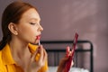 Closeup face of sexy young woman with red hair applying lipstick holding mirror and looking at herself. Close up of Royalty Free Stock Photo