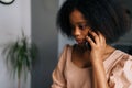 Closeup face of thoughtful young African American woman talking on smartphone at home. Close up portrait of attractive Royalty Free Stock Photo