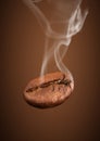 Closeup falling coffee bean with smoke on brown background Royalty Free Stock Photo