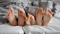 Closeup of family bare feet lying together on bed under blanket Royalty Free Stock Photo