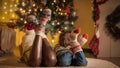 Closeup of family feet in knitted wool socks lying next to glowing Christmas tree in living room. Pure emotions of Royalty Free Stock Photo