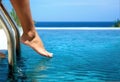 Closeup of female barefoot legs testing swimming pool temperature in sun day with blur background.